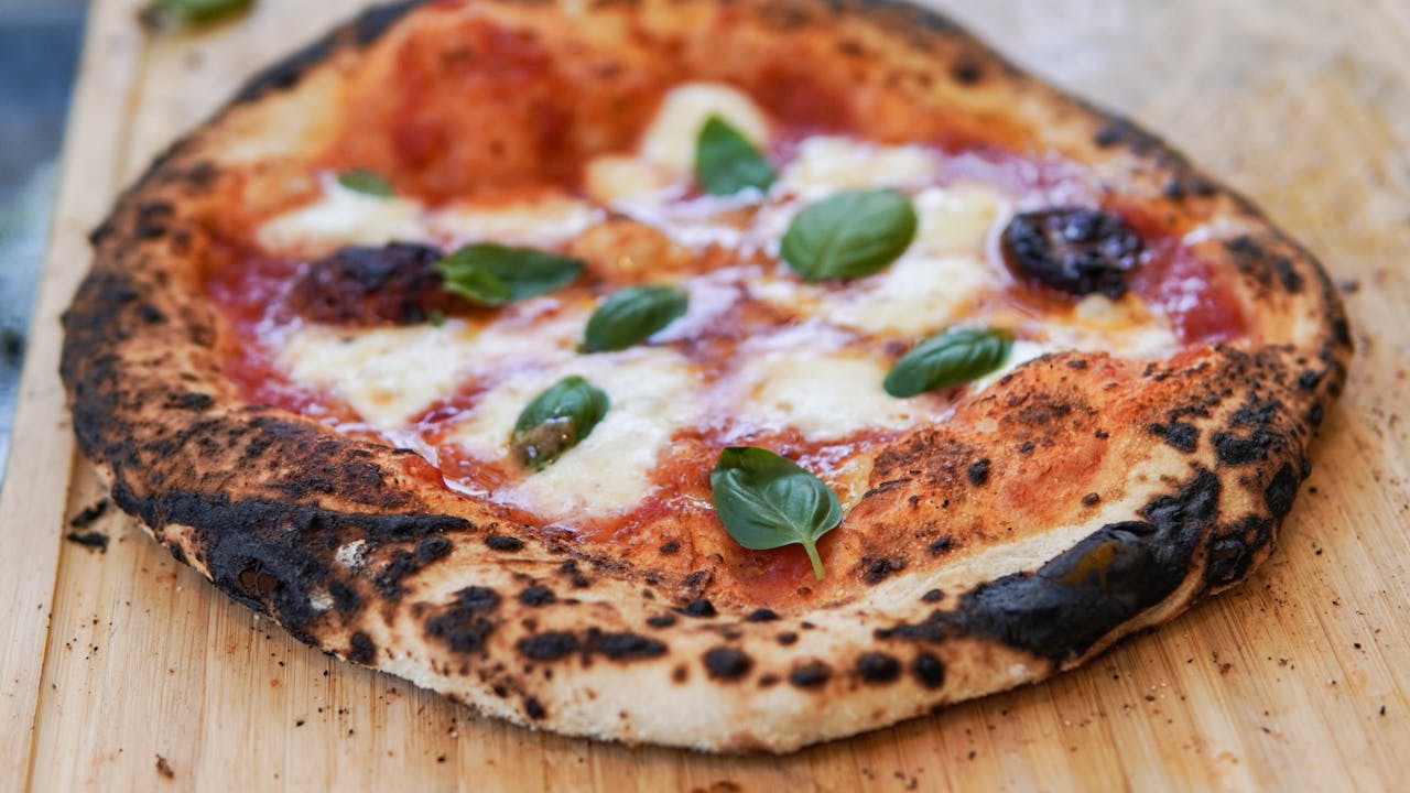 Close-up of a wood-fired Margherita pizza with fresh basil on a wooden surface.
